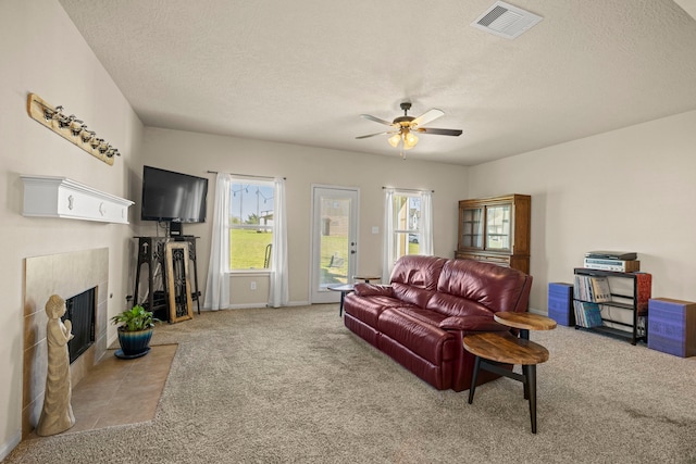 living area with visible vents, a ceiling fan, a textured ceiling, carpet, and a tile fireplace