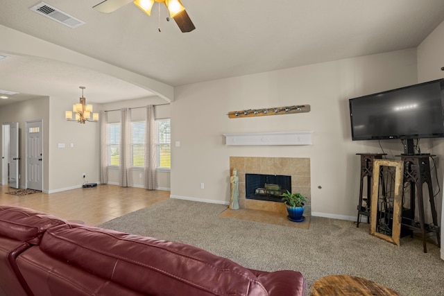 carpeted living room with visible vents, baseboards, a tile fireplace, and ceiling fan with notable chandelier