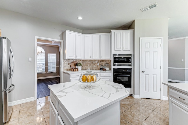 kitchen featuring visible vents, backsplash, a center island, white cabinetry, and stainless steel appliances