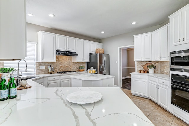 kitchen featuring range hood, light tile patterned floors, a sink, stainless steel appliances, and white cabinetry