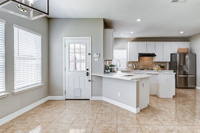 kitchen featuring light tile patterned floors, stainless steel appliances, tasteful backsplash, and a peninsula