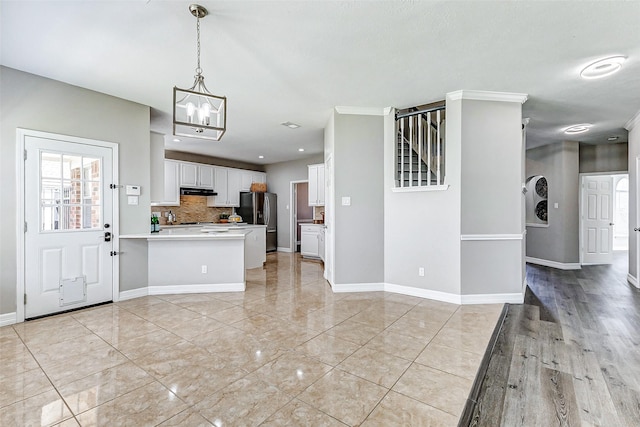 kitchen featuring a peninsula, an inviting chandelier, decorative backsplash, white cabinets, and stainless steel fridge