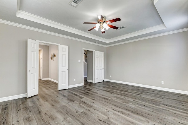 unfurnished bedroom featuring a tray ceiling, visible vents, and wood finished floors