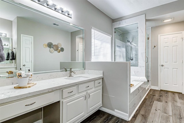 full bath featuring visible vents, wood finished floors, a marble finish shower, a bath, and vanity