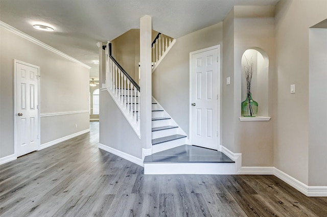 staircase with crown molding, wood finished floors, arched walkways, and baseboards