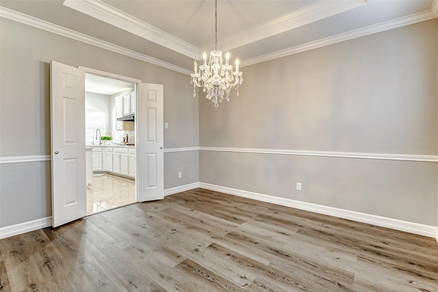 empty room with an inviting chandelier, a tray ceiling, baseboards, and light wood finished floors