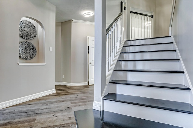 stairway with baseboards, wood finished floors, and ornamental molding