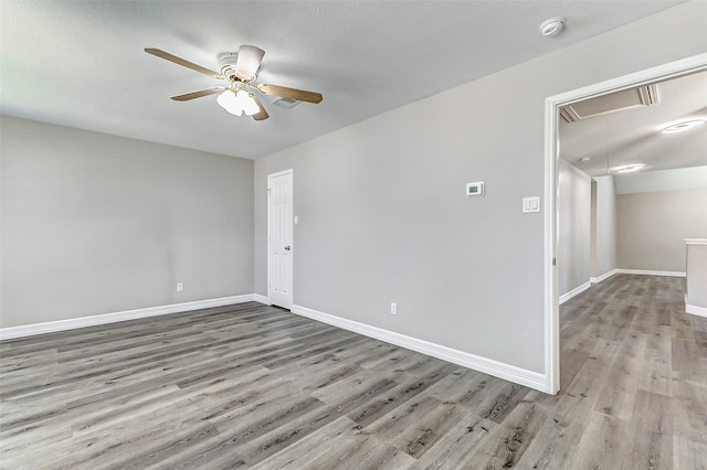 spare room with attic access, light wood-style flooring, a ceiling fan, and baseboards