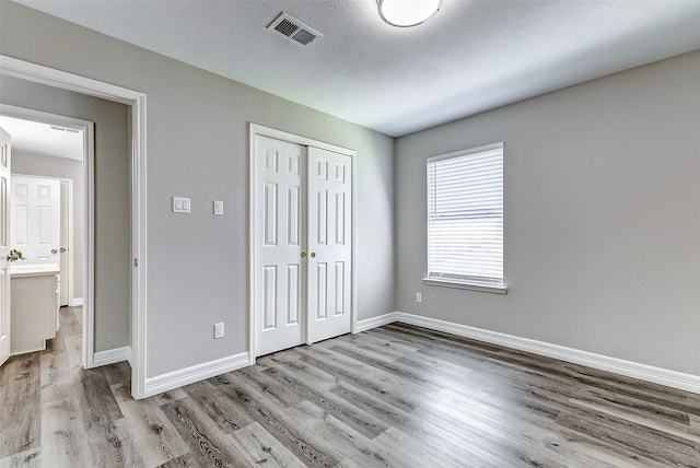 unfurnished bedroom featuring visible vents, baseboards, a closet, and wood finished floors