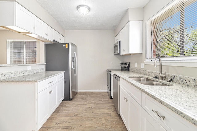 kitchen with light wood-style flooring, a sink, a textured ceiling, appliances with stainless steel finishes, and white cabinets