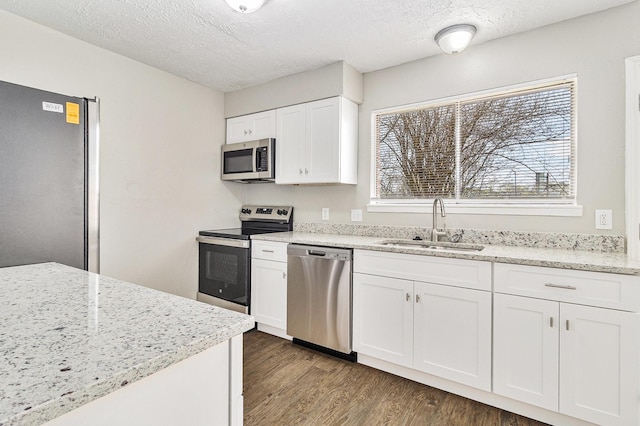 kitchen featuring light stone countertops, appliances with stainless steel finishes, wood finished floors, white cabinets, and a sink