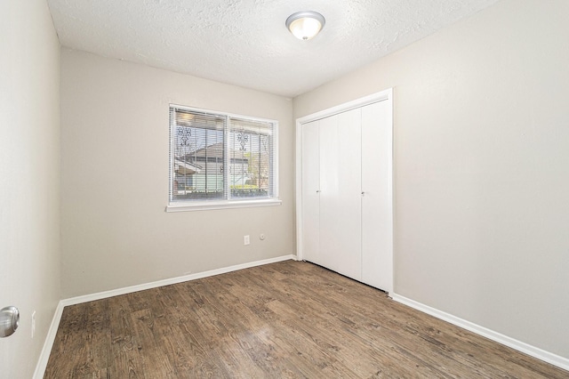 unfurnished bedroom featuring wood finished floors, baseboards, a closet, and a textured ceiling