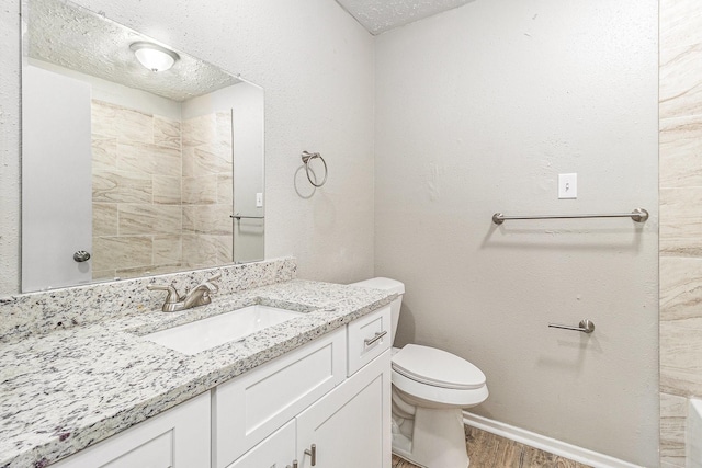 full bathroom featuring toilet, a textured ceiling, wood finished floors, baseboards, and vanity