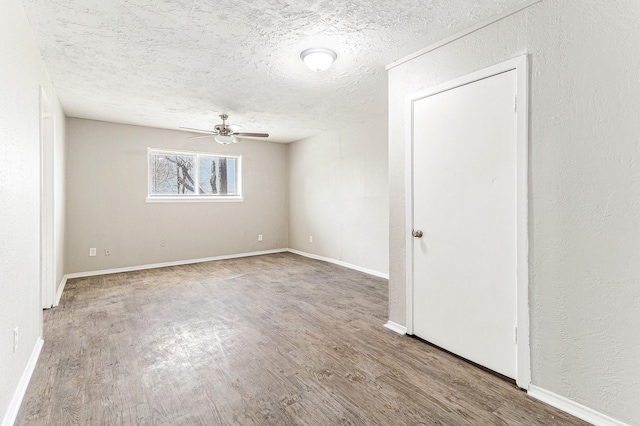 spare room featuring baseboards, a textured ceiling, wood finished floors, and a ceiling fan