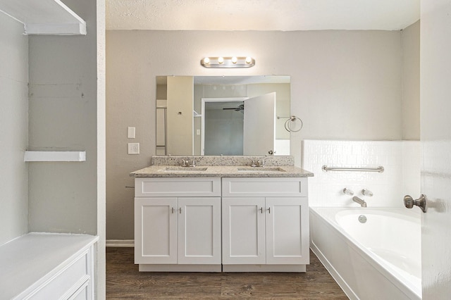 full bathroom with a sink, a garden tub, wood finished floors, and double vanity