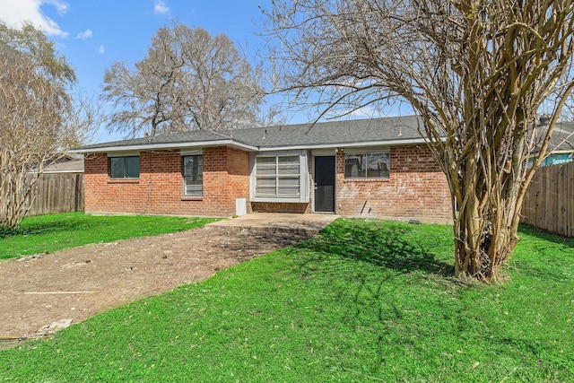 view of front facade with brick siding, a shingled roof, a front yard, and fence