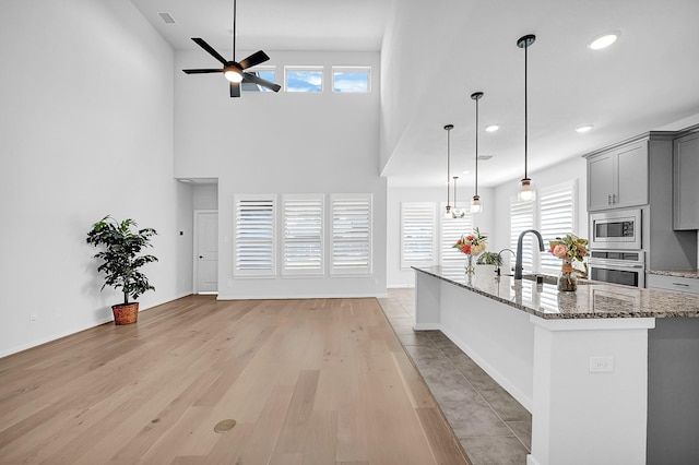 kitchen with ceiling fan, gray cabinets, appliances with stainless steel finishes, stone countertops, and a sink