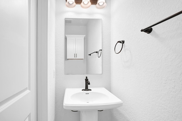 bathroom with a textured wall, visible vents, and a sink