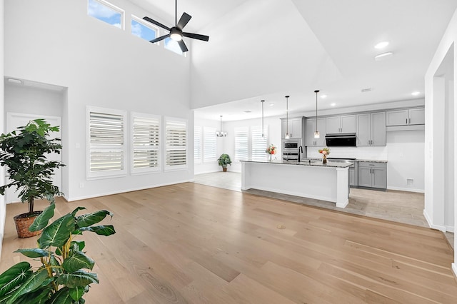 unfurnished living room with recessed lighting, ceiling fan with notable chandelier, light wood-style flooring, and baseboards