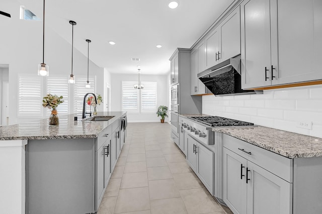 kitchen with an island with sink, a sink, under cabinet range hood, appliances with stainless steel finishes, and decorative backsplash