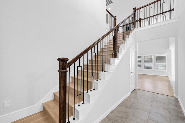 stairs featuring tile patterned flooring, baseboards, and a towering ceiling