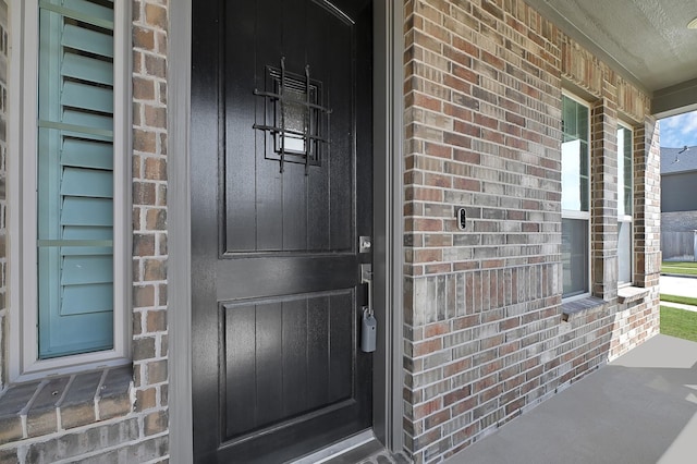 doorway to property featuring a porch and brick siding