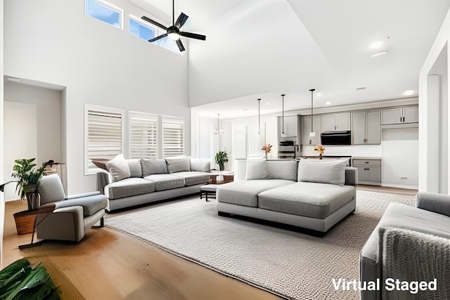 living area featuring a towering ceiling, a ceiling fan, and light wood finished floors