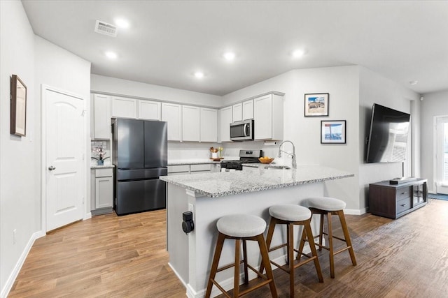 kitchen featuring a kitchen bar, light stone counters, a sink, appliances with stainless steel finishes, and a peninsula