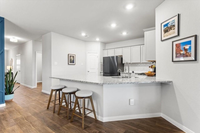 kitchen featuring white cabinetry, a peninsula, wood finished floors, and freestanding refrigerator