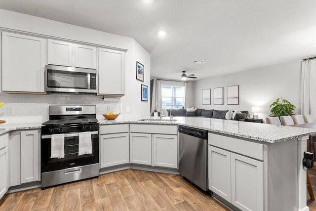 kitchen with light wood-style flooring, open floor plan, stainless steel appliances, a peninsula, and ceiling fan