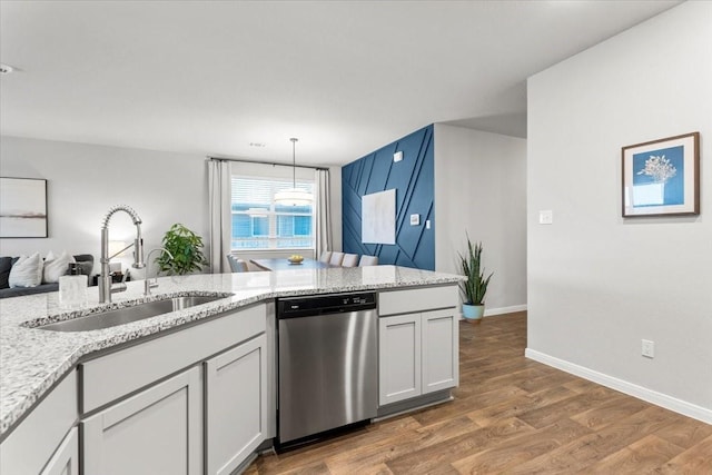 kitchen featuring baseboards, light stone countertops, stainless steel dishwasher, wood finished floors, and a sink