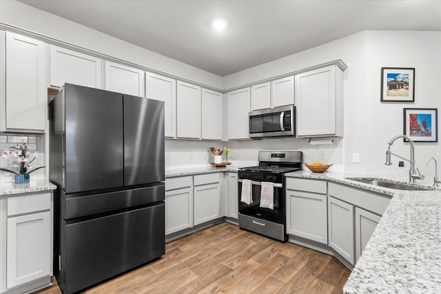 kitchen featuring a sink, backsplash, stainless steel appliances, light wood finished floors, and light stone countertops