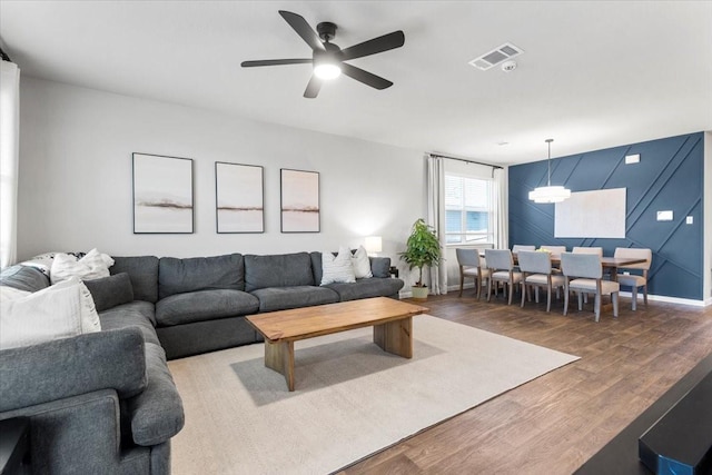 living area featuring baseboards, wood finished floors, visible vents, and ceiling fan