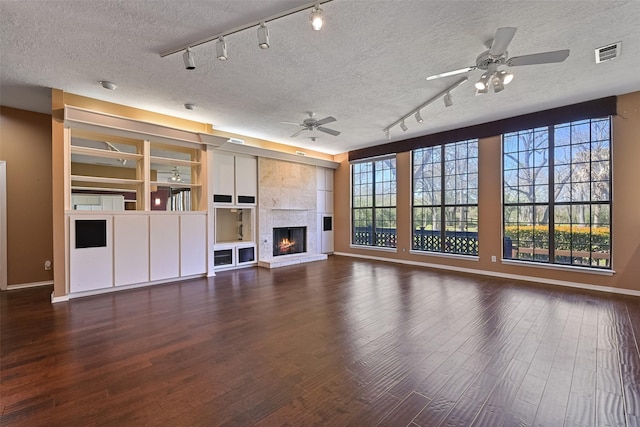 unfurnished living room featuring visible vents, plenty of natural light, wood finished floors, a fireplace, and ceiling fan