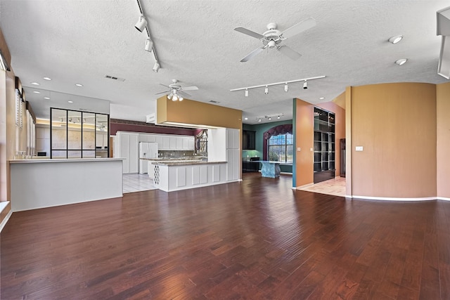 unfurnished living room featuring visible vents, track lighting, a textured ceiling, light wood-style floors, and ceiling fan