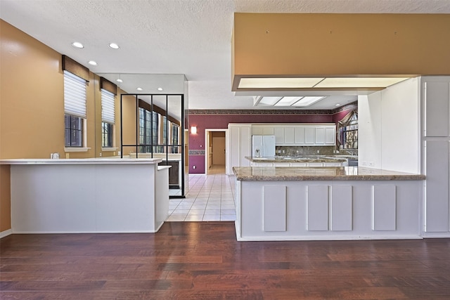 kitchen with a peninsula, light wood-style flooring, white cabinets, white refrigerator with ice dispenser, and a textured ceiling