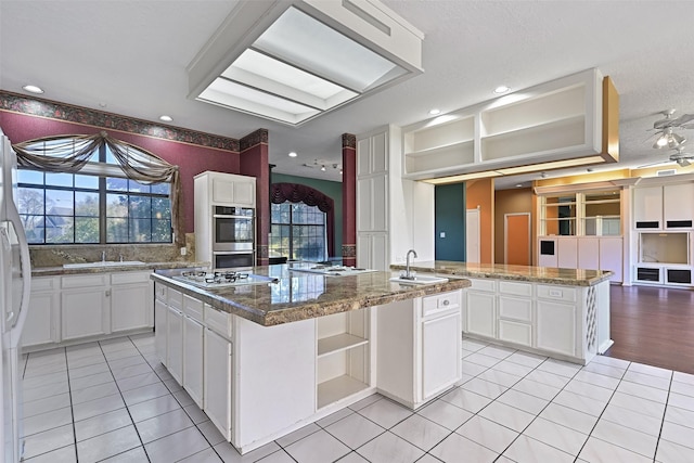 kitchen with double oven, open shelves, plenty of natural light, and a center island with sink