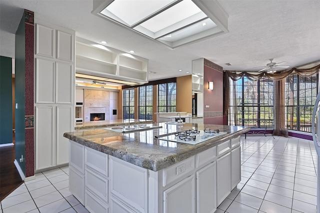 kitchen featuring light tile patterned floors, a warm lit fireplace, open floor plan, and a ceiling fan