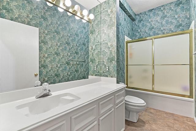 bathroom with wallpapered walls, toilet, vanity, combined bath / shower with glass door, and a textured ceiling