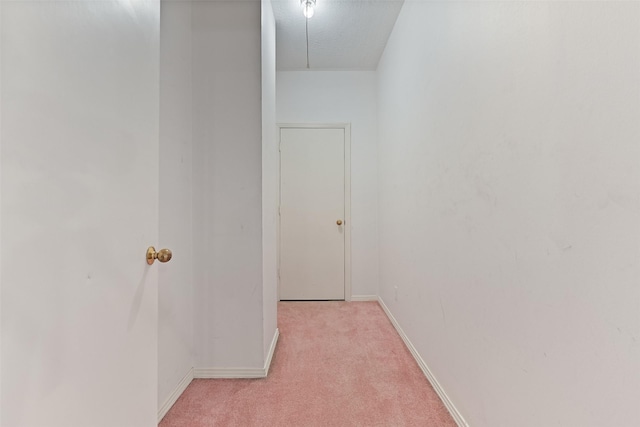 hall with attic access, light colored carpet, and baseboards