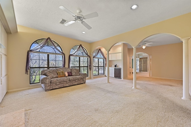 living area with a ceiling fan, visible vents, ornate columns, arched walkways, and light colored carpet