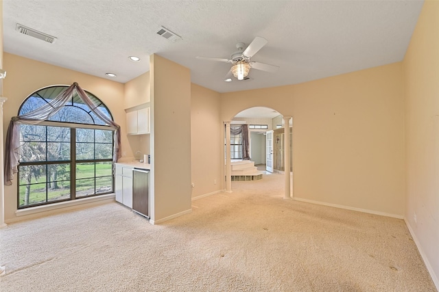 spare room with a ceiling fan, arched walkways, visible vents, and light colored carpet