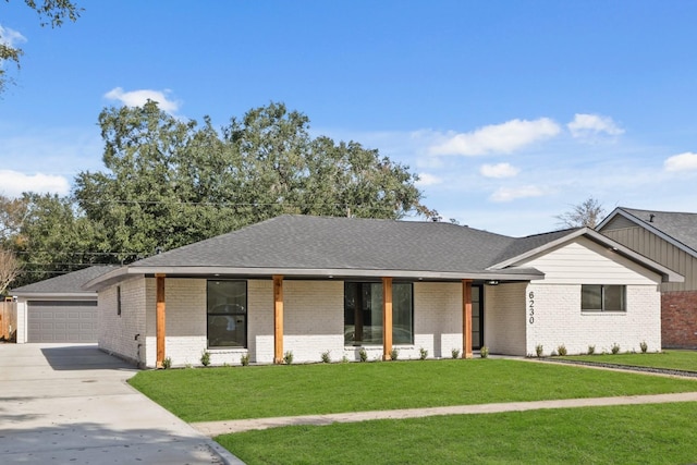 view of front facade featuring driveway, roof with shingles, a front yard, a garage, and brick siding