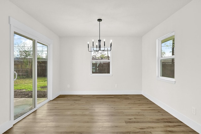 unfurnished dining area with an inviting chandelier, wood finished floors, baseboards, and a wealth of natural light