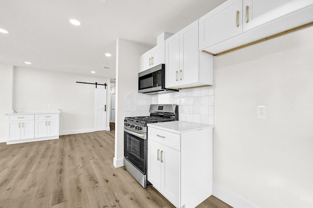 kitchen with decorative backsplash, a barn door, white cabinetry, and appliances with stainless steel finishes