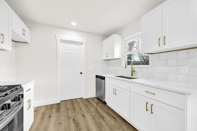 kitchen featuring light stone countertops, light wood-type flooring, decorative backsplash, appliances with stainless steel finishes, and a sink