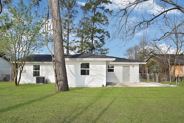 back of property with central air condition unit, a lawn, and fence