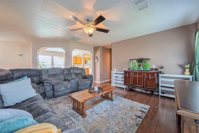 living area featuring arched walkways, visible vents, a ceiling fan, and dark wood-style flooring