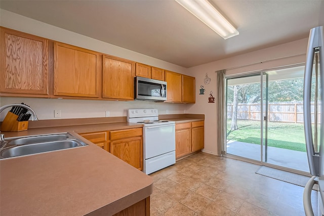 kitchen with a sink, stainless steel microwave, light countertops, and white range with electric stovetop