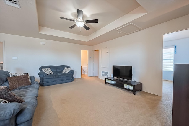 carpeted living area featuring visible vents, a raised ceiling, attic access, and a ceiling fan